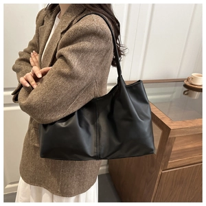 Detail of a large black PU leather tote bag with stylish pleated texture and contrast stitching