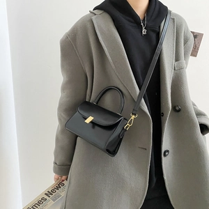 Minimalistische schwarze Umhängetasche mit goldener Schnalle am grauen Wollmantel