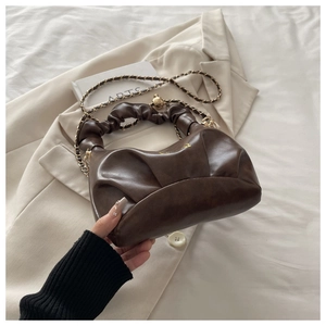 Detail of dark brown ruched dumpling bag featuring gold chain strap and supple texture