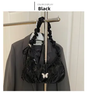 Detail of black glossy crinkled bag with silver butterfly buckle and ruffled strap