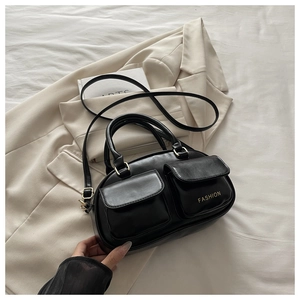 Detail of black bowling bag with dual front pockets and gold hardware on beige blazer