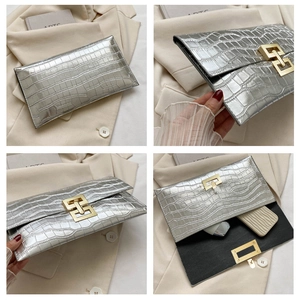 Detail view of silver crocodile pattern clutch bag featuring a gold geometric metal buckle