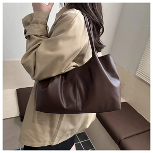 Close-up of a minimalist dark brown leather tote bag worn as a shoulder bag on a trench coat