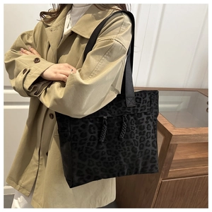Detail of leopard print tote bag with black decorative knots worn on khakis trench coat