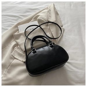 Close-up of black bowling bag with gold hardware and fine stitching on a beige suit