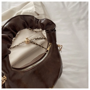 Close-up of ruched handle and leather chain strap with gold ball charm on brown bag