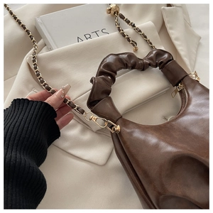 Detail of a brown leather handbag with pleated handle and golden chain strap on a white blazer