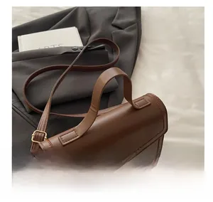 Close-up of matte brown square crossbody bag with gold metal buckle on grey blazer