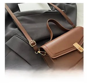 Detail of a brown leather crossbody bag featuring gold buckle and decorative stitching