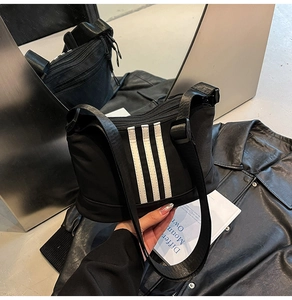 Dettaglio macro della borsa a tracolla in nylon nero con tre strisce bianche verticali e tracolla