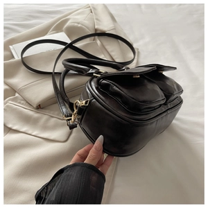 Detail of matte black crossbody bag with dual front pockets and gold-tone hardware