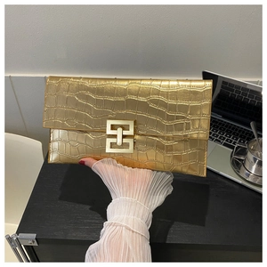 Detail of gold envelope clutch bag featuring crocodile embossing and geometric metal buckle