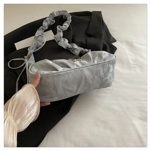 Close-up of silver pleated crescent bag featuring a golden metal bow and cloud texture