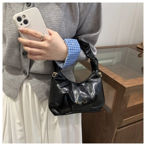 Detail showing high-gloss black ruched handbag with golden logo and ruffled handle
