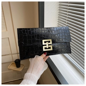 Close-up of black crocodile texture envelope clutch bag with gold interlocking metal clasp