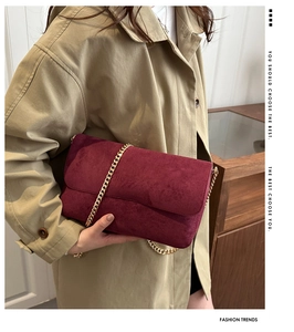 Close-up of elegant burgundy suede shoulder bag with chic gold metal chain strap