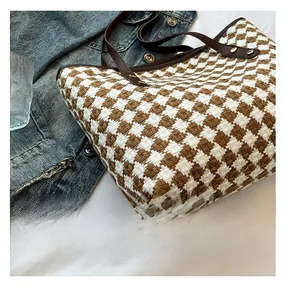 Detail of checkered woven tote bag with brown leather straps and gold rivet accents