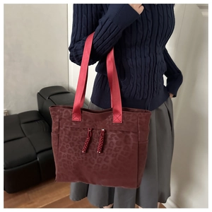 Détail du grand sac cabas léopard rouge avec pompons porté par un mannequin en décor maison