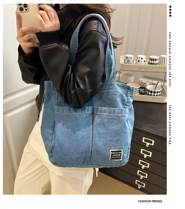 Close-up of denim tote bag featuring dual front pockets and white logo patch detail