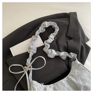 Close-up of silver pleated crescent bag with bow detail and metallic texture finish