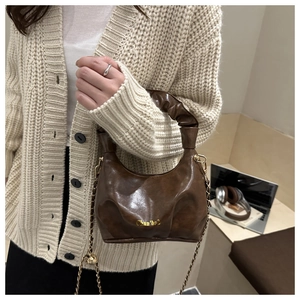 Detail of a brown ruched shoulder bag featuring a sleek gold chain strap and logo