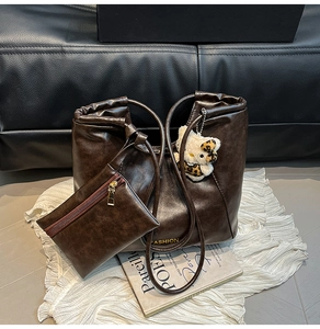 Detail of dark brown leather tote bag with a plush bear charm and matching pouch