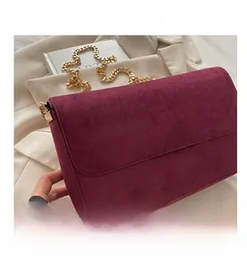 Close-up of a burgundy suede crossbody bag featuring a golden chain strap and flap design