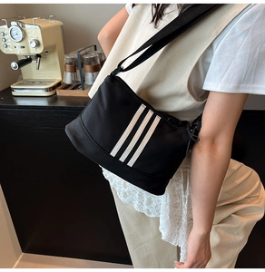 Vista laterale di borsa a tracolla in nylon nero con tre strisce bianche su modella