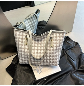 Close-up of gray houndstooth woven tote bag with silver rivets and leather straps