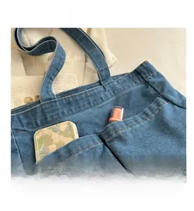 Detail of blue denim tote bag showing front pockets holding a phone case and lipstick