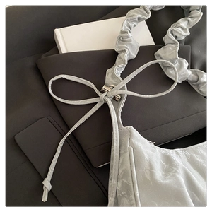 Detail view of silver crescent bag featuring bow detail and ruffled cloud shoulder strap