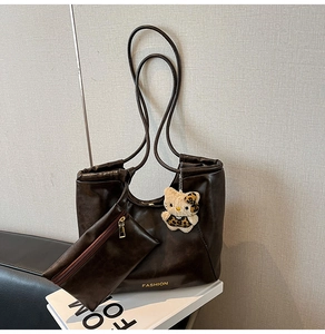 Detail of dark brown tote bag with gold lettering, small clutch and leopard plush charm