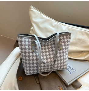 Close-up of woven houndstooth tote with grey leather handles and gold rivet details
