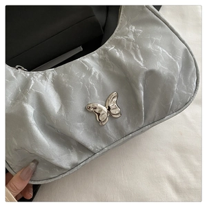 Close-up of silver pleated crescent bag with 3D metallic butterfly detail and Y2K aesthetic