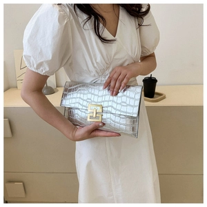 Detail of silver crocodile pattern clutch with gold geometric lock held by a model