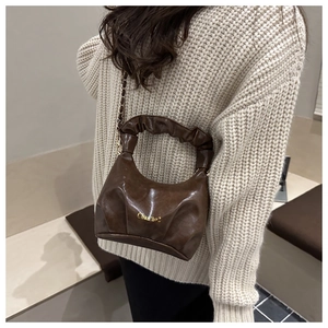 Detail of dark brown pleated handbag with gold hardware and chain strap on a knit sweater