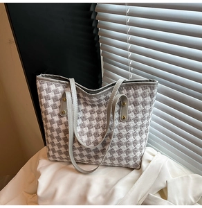 Detail of woven houndstooth tote bag with grey leather straps and gold metal rivets