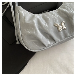 Detail of silver pleated hobo bag with a metallic butterfly emblem and textured finish