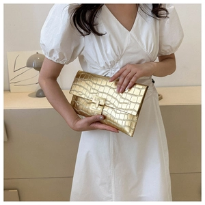 Close-up of golden envelope clutch featuring crocodile pattern and H-shaped metal buckle