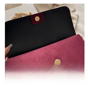 Detail of golden magnetic clasp on a wine red suede flap bag with chain strap