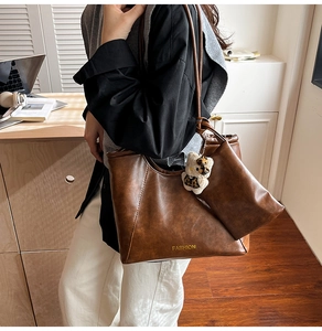 Detail of vintage brown leather tote bag set with golden fashion text and bear charm