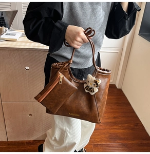 Detail view of large brown tote bag with leather texture, coin purse, and cat charm