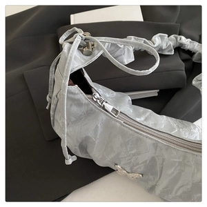 Macro detail of the silver pleated texture and butterfly hardware on the crescent bag