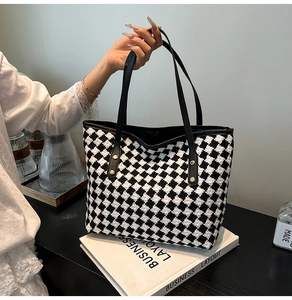 Close-up of woven houndstooth tote bag featuring black leather handles and gold studs