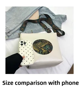 Detail view of cream vintage crossbody bag with elephant patch next to a smartphone