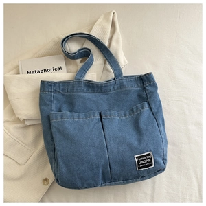 Detailed flat lay of a blue denim tote bag with dual front pockets and black logo patch