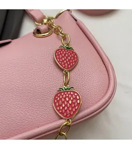 Detailed close-up of pink crossbody bag featuring strawberry charms on a gold chain strap