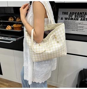Close-up of woven checkerboard tote bag with white leather straps and gold rivets
