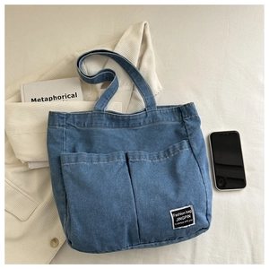 Detail of blue washed denim tote bag showing two front pockets and woven brand label