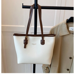 Detail of a large white tote bag with brown leather trim and adjustable buckle strap